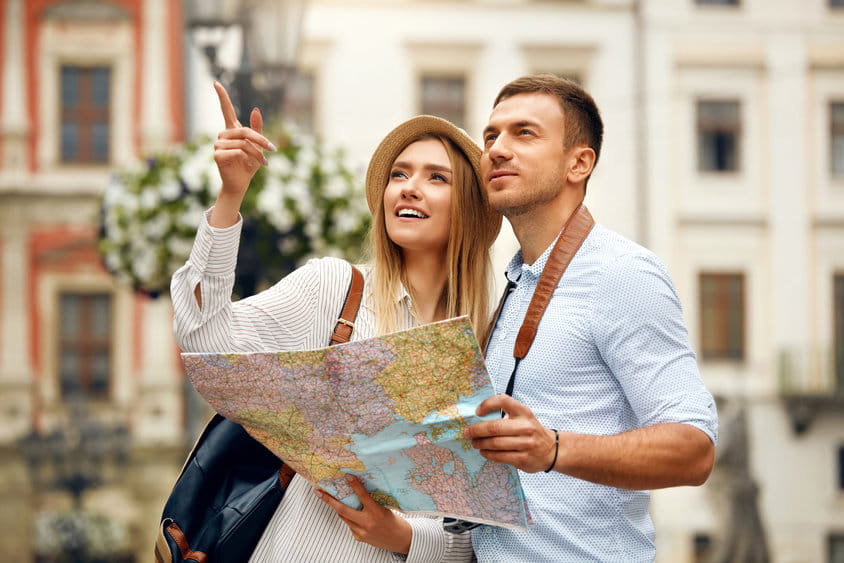 Couple With Map On Travel Vacations, Sightseeing. Happy Tourist Man And Woman In Stylish Clothes Traveling On Weekend, Walking With Map Around Streets. Tourism Concept. High Quality Image.