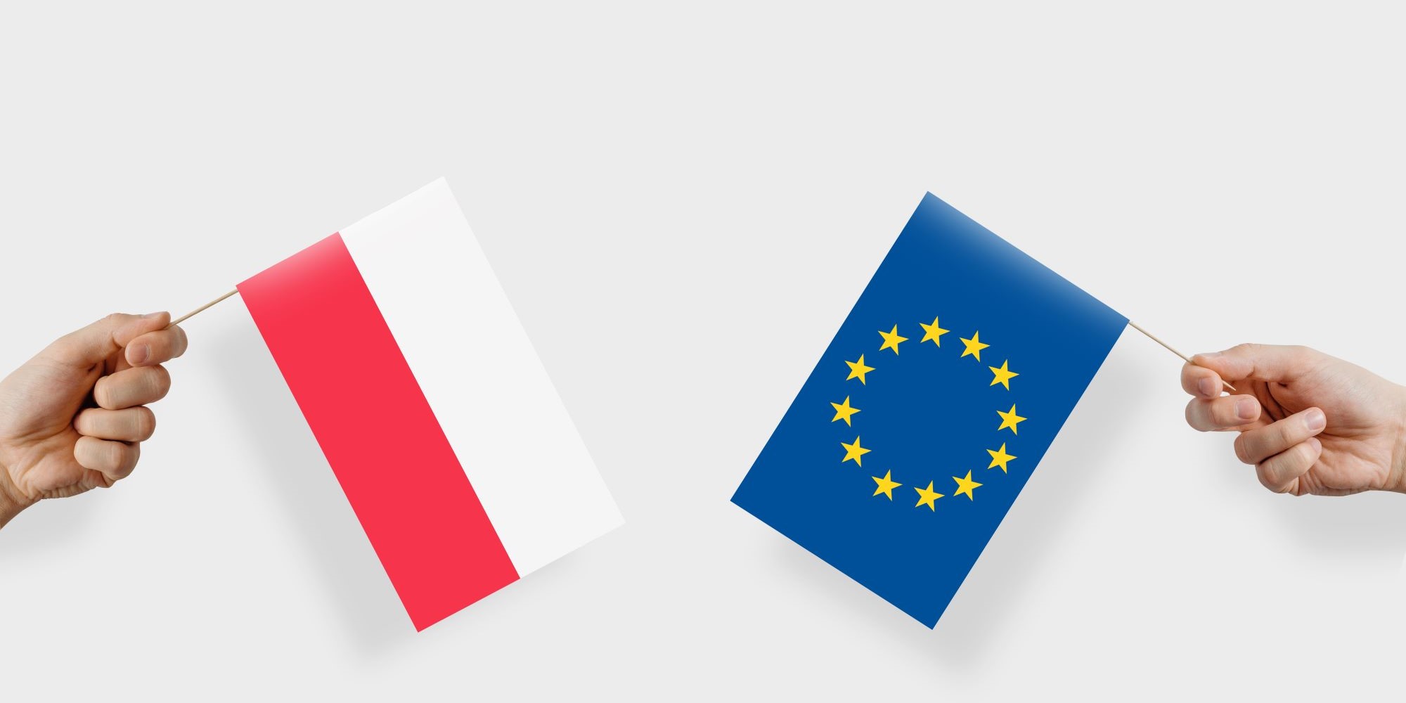 Dłonie z małymi flagami Polski i Unii Europejskiej.