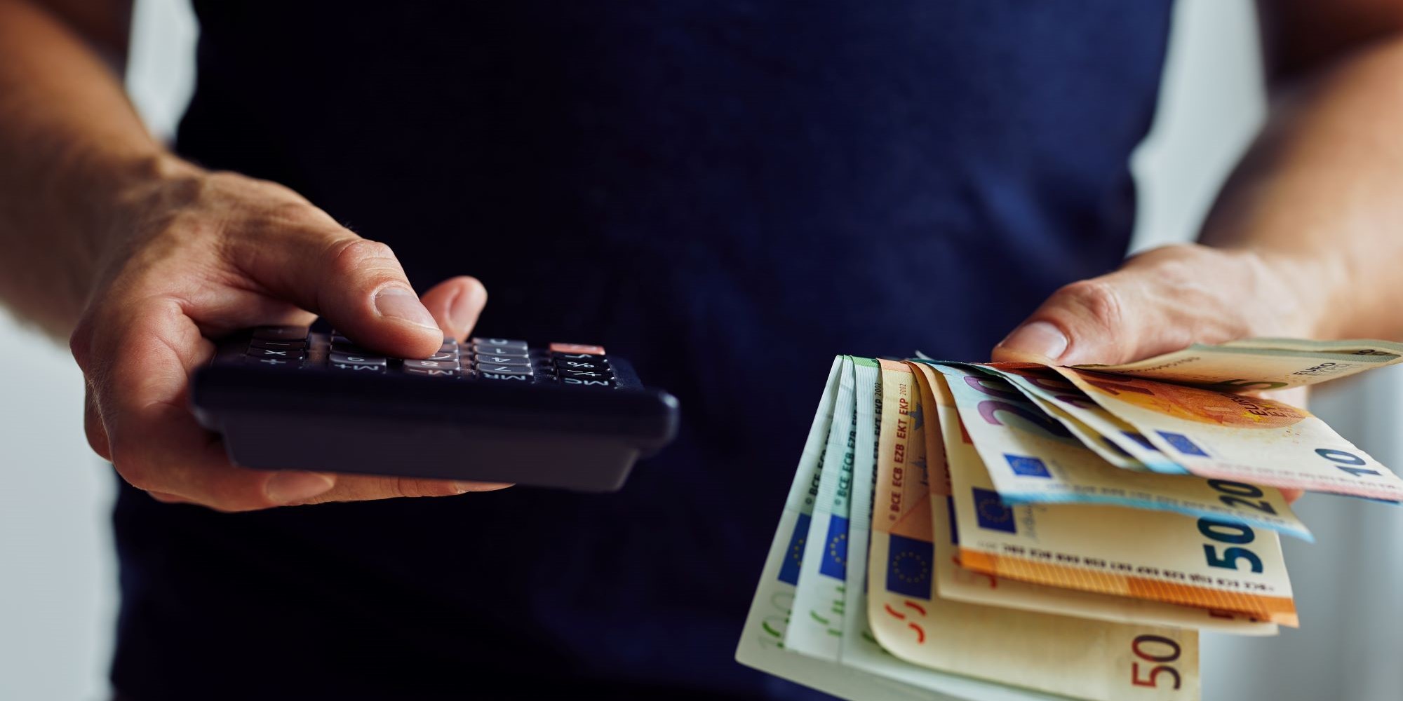 Mężczyzna trzyma kalkulator i plik banknotów euro