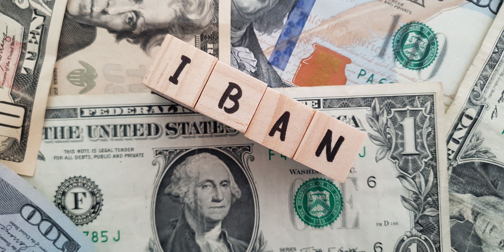 Tekst IBAN ułożony z klocków, w tle banknoty różnych walut