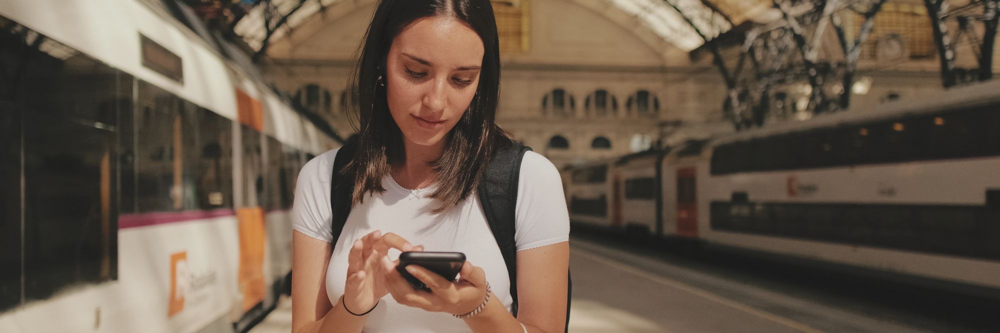 Kobieta na peronie dworca sprawdza informacje w internecie na telefonie